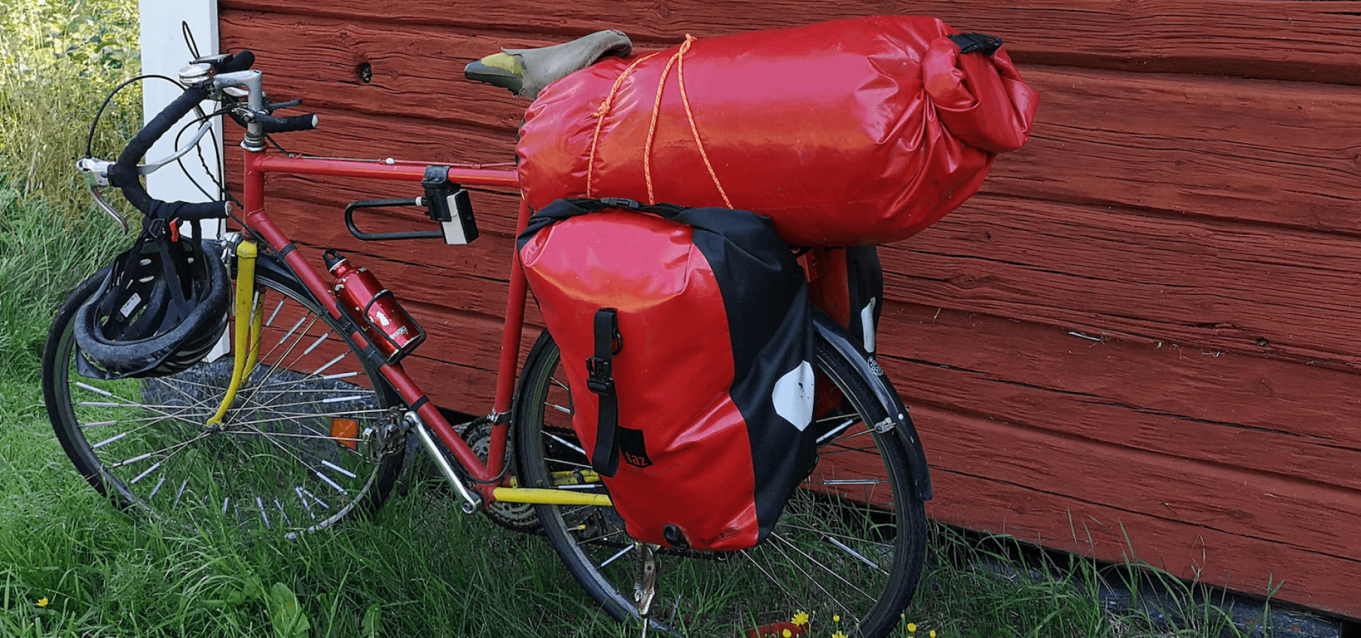 Röd cykel med packning lutad mot en röd trävägg - Foto Hyttan