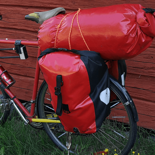 Röd cykel med packning lutad mot en röd trävägg - Foto Hyttan