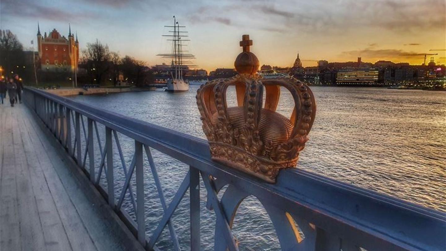 Kunglig krona på broräcke med Skeppsholmen i bakgrunden 